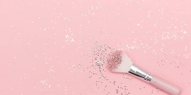 Makeup brush and shiny sparkles on pastel pink background. Festive magic makeup concept. Template for design, Top view Flat Lay Copy space.